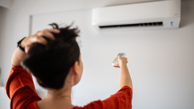 Mulher de camisola laranja a ligar o aparelho de ar condicionado.